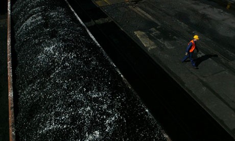 A worker walks past freshly-mined, high quality coal awaiting transport on a tra