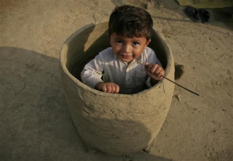 An internally displaced child sits in a mud oven outside his family tent at a ca